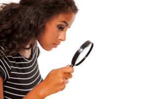 Beautiful young dark skinned woman looking trough the magnifying glass